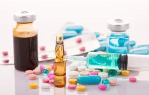 Tablets, capsules, glass vials, bottles and a syringe on a surface, showing medicines to keep away from children
