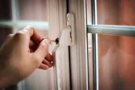 A hand turning a small key in the lock of a white window frame, showing how windows are locked at home