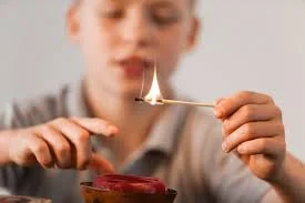 A boy lights a match over a small dish, showing the danger of children playing with matches