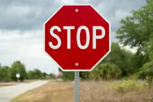 Red octagonal STOP sign with white letters on a metal pole beside a road, showing the sign that means stop moving