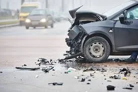 Dark car with a crushed front end on a road, broken parts scattered on the tarmac after a road accident
