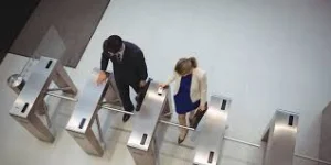 Seen from above, a man in a dark suit and a woman in a white jacket walk through turnstile gates at an office entrance