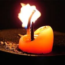 A lit orange candle with a bent wick and bright flame, showing how a burning candle can cause fire