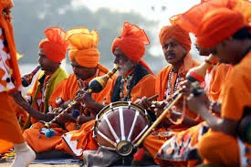 Group of men in orange turbans and clothes playing drums and wind instruments outdoors