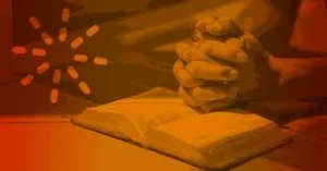 Clasped hands resting on an open Bible, shown in orange tones, to introduce prayer