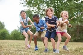 Four smiling children pulling on a rope together outdoors on grass, a game that shows teamwork