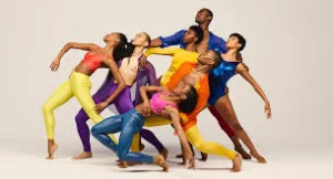 Group of dancers in bright colourful costumes leaning together in a modern dance pose