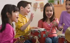 Four smiling children playing drums and hand percussion together in a classroom