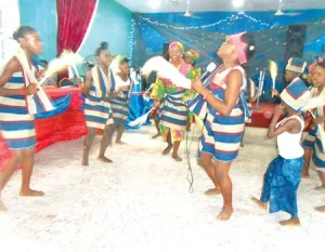 Dancers in striped blue and white outfits performing a group dance in a decorated hall, some holding cloths