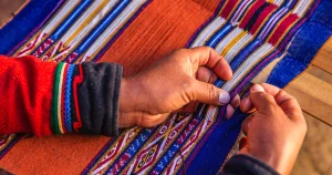 Hands weaving a colourful striped cloth in red, blue, orange and white patterns