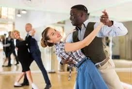 A man and a woman smiling as they dance together as a pair, with other couples behind them