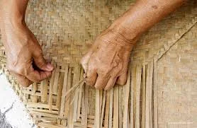 Close view of hands weaving flat dried strips into a mat