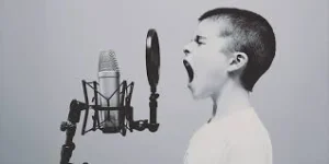 Black and white photo of a boy singing loudly into a studio microphone with a pop filter