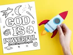 Colouring page reading God Is Powerful with space drawings, next to a hand holding a paper rocket