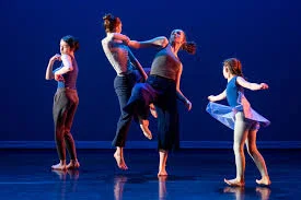 Four barefoot dancers moving freely on a dark stage, each in a different pose
